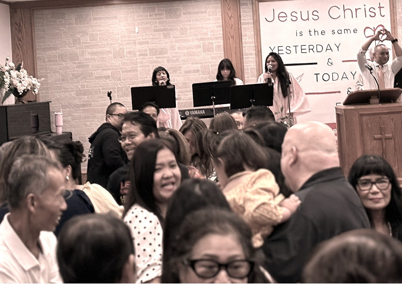 Sunday worship at New International Church, Garland, Texas — congregation gathered with worship team and 'Jesus Christ is the same yesterday and today' banner